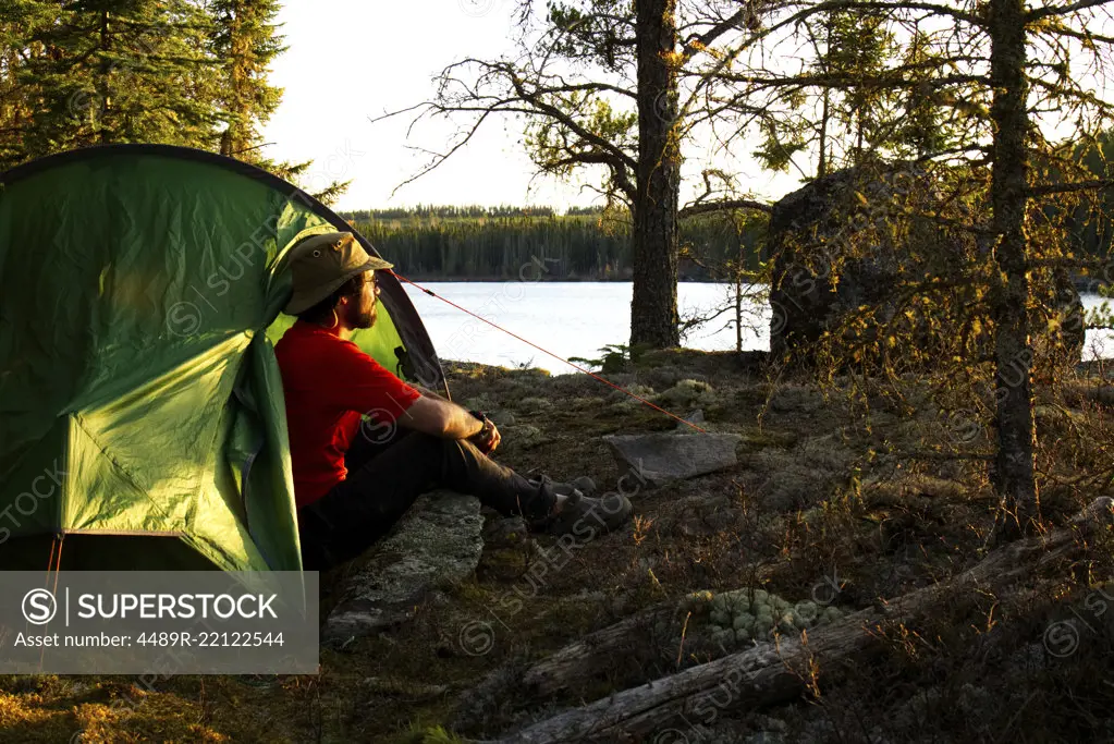a single male sitting by a tent close to the water on a rocky shore in Ontario Canada. 