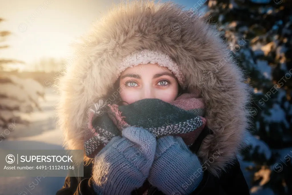 Young attractive female in warm clothing with fur joyful laughing beside covered snow conifer tree
