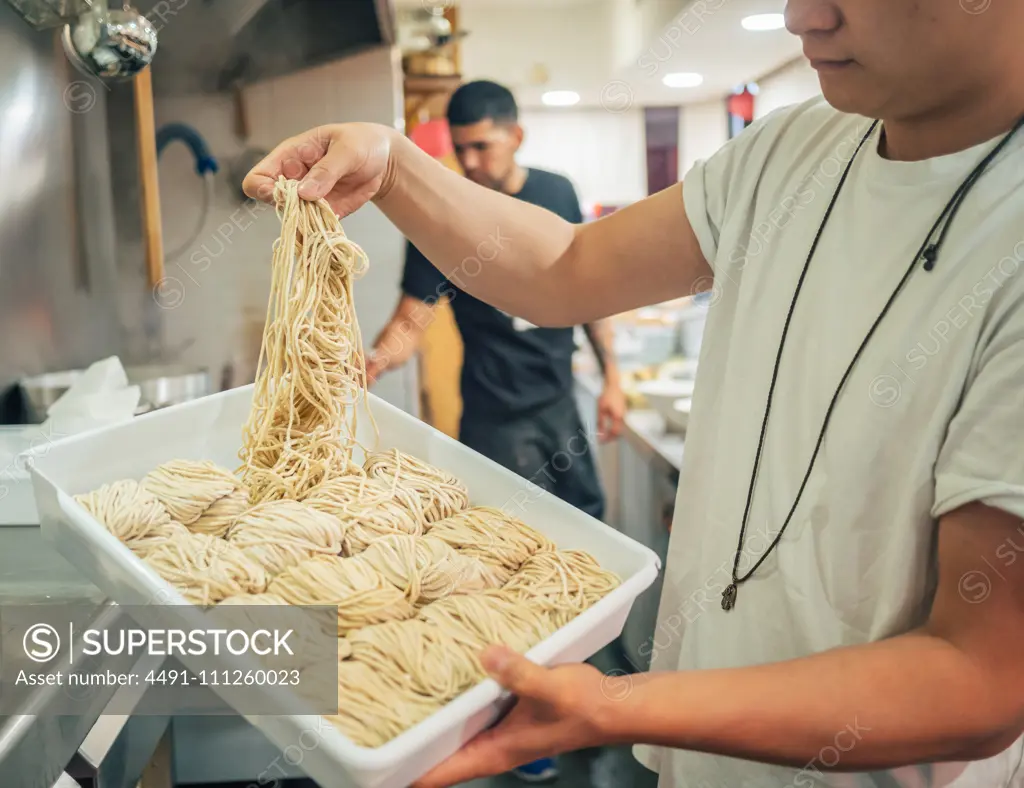 Side view of young multiracial men taking noodles from tray in restaurant