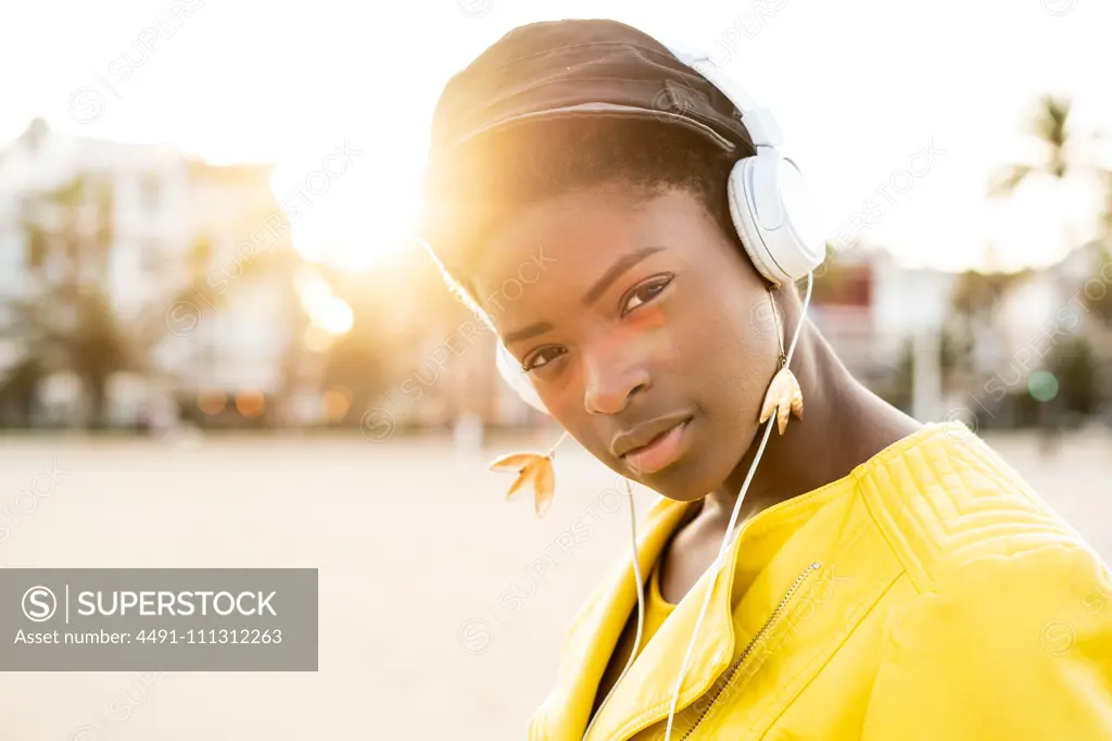 Portrait of African American woman in stylish bright jacket looking at camera on sandy beach blurred background  millennial