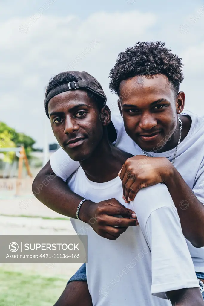 Cheerful hugging African American young men looking at camera and gesturing