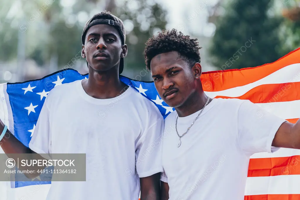 Serious African American men holding American flag on shoulder and looking away