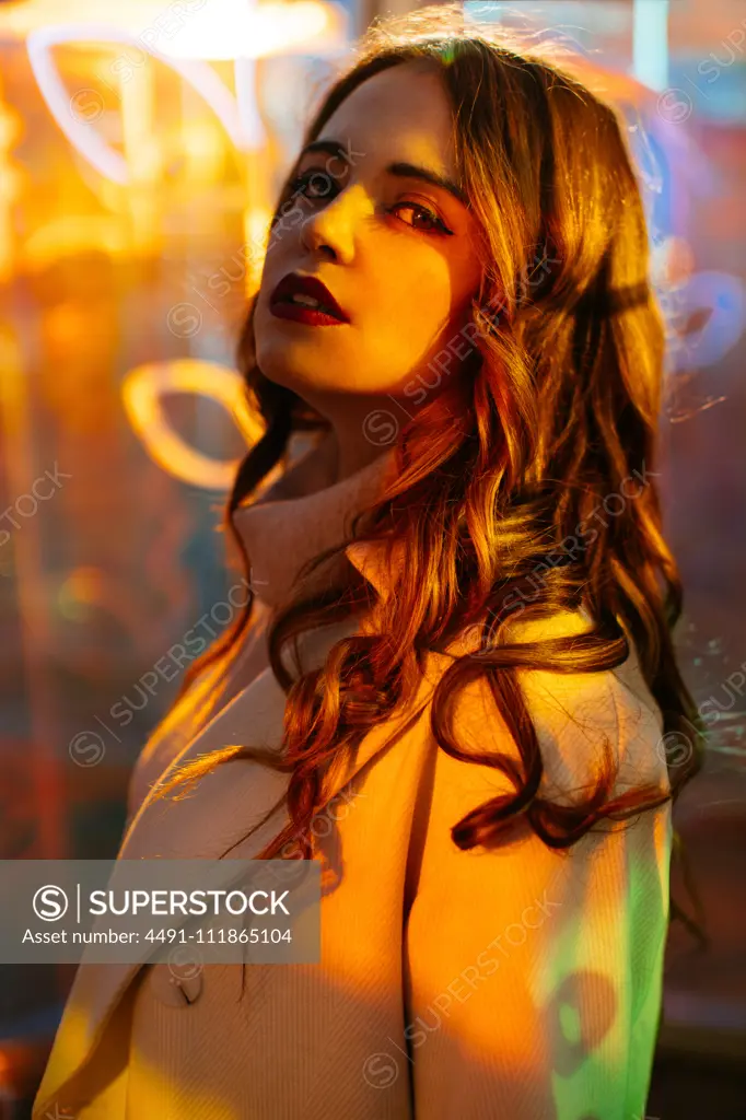 Sensual young woman in coat in light of neon signs