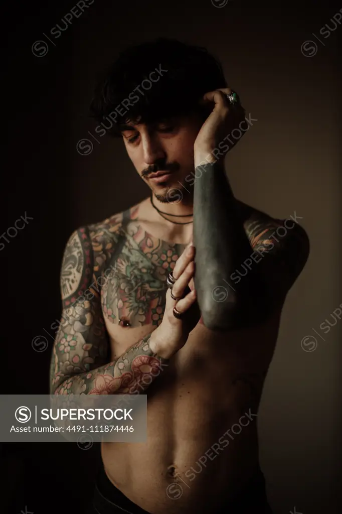 Handsome shirtless tattooed man with mustache and pierced ears and nipples with closed eyes