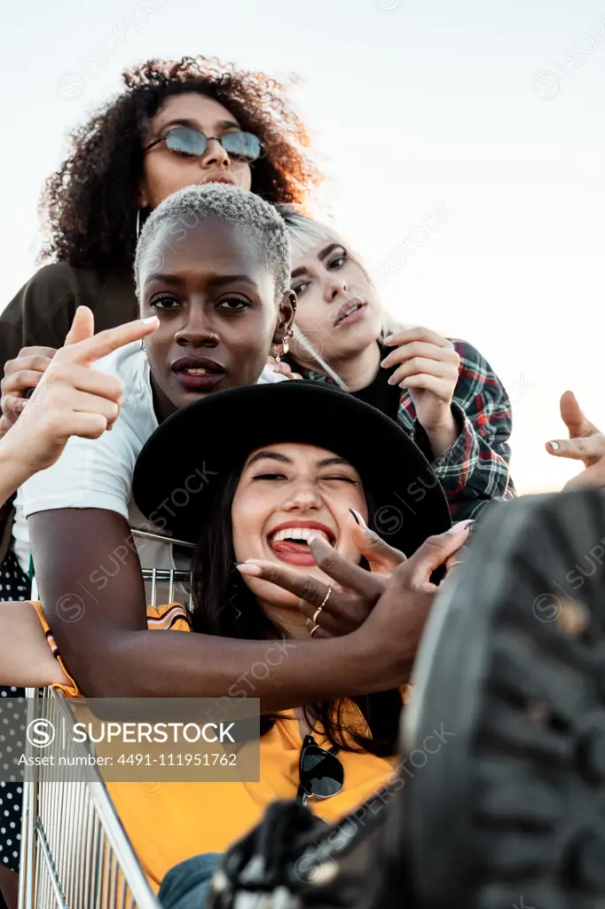 Multiracial group of young women standing around shopping cart on road