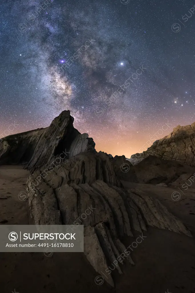 From below of rough cliff peak under milky way colorful blue night sky and shiny stars on background