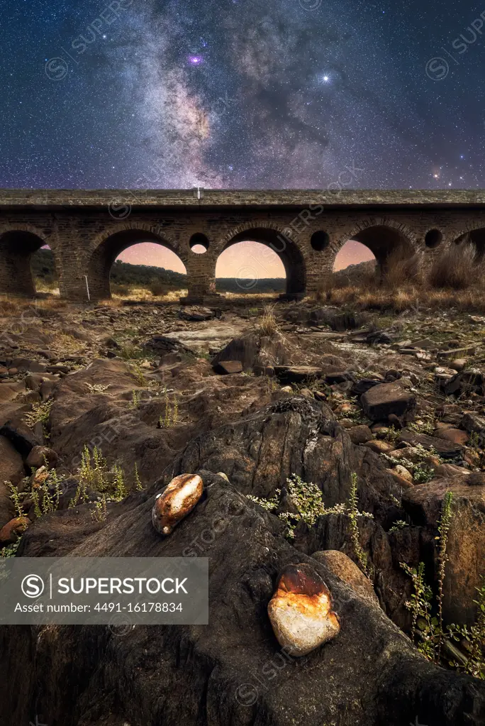 Rocky ground and old stone bridge with colorful night sky with milky way and stars on background