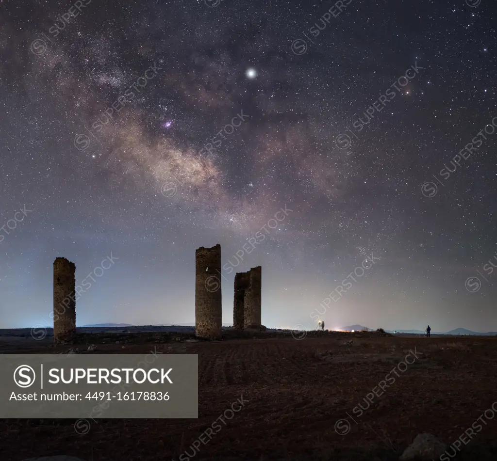 Ancient stone towers on empty sandy ground under dark starry sky with milky way