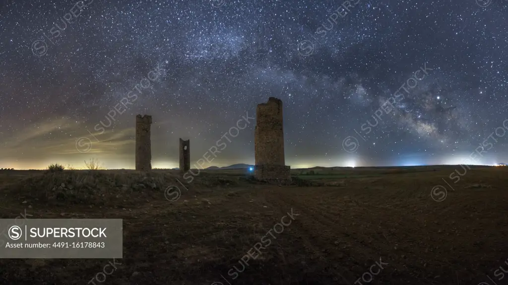 Ancient stone towers on empty sandy ground under dark starry sky with milky way