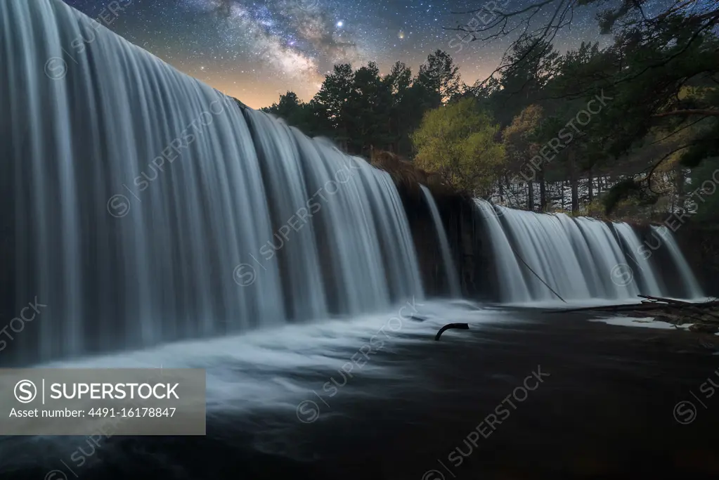 Beautiful powerful rocky waterfall and stream of water with colorful night starry sky on background