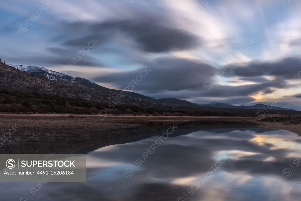Long exposure picturesque view of cloudy sundown sky over mountain and peaceful lake water in nature