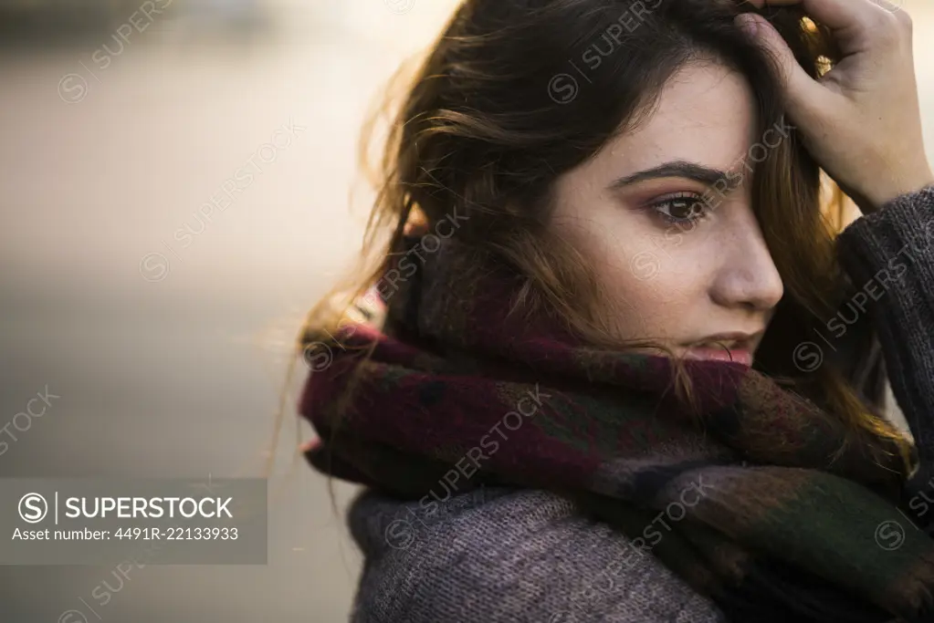 Portrait of young woman standing in warm clothes touching her face.