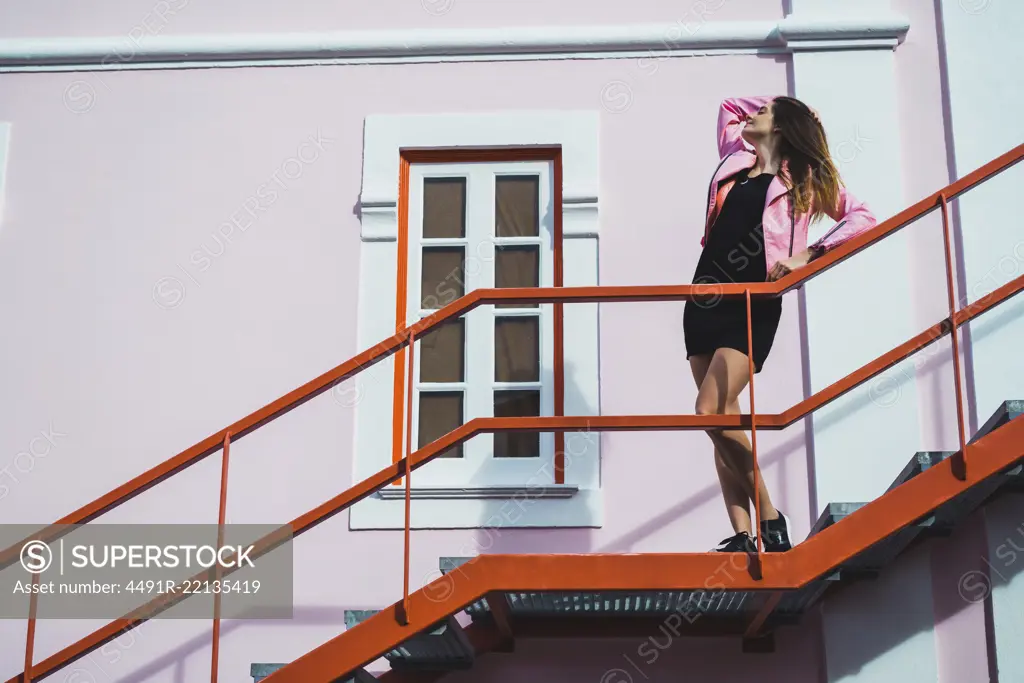 Side view of young attractive woman standing and posing on stairs on street.