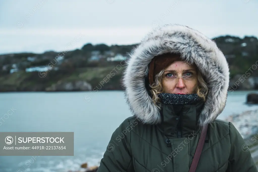 Pretty tourist woman in warm clothes looking at camera on background of hills and sea.