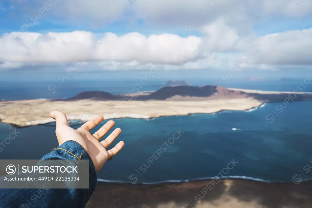 Hand of unrecognizable tourist showing small island in blue sea in Lanzarote, Spain.