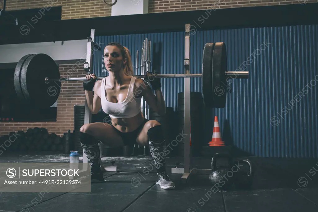 Fit blonde woman training lifting a bar weights in gym 