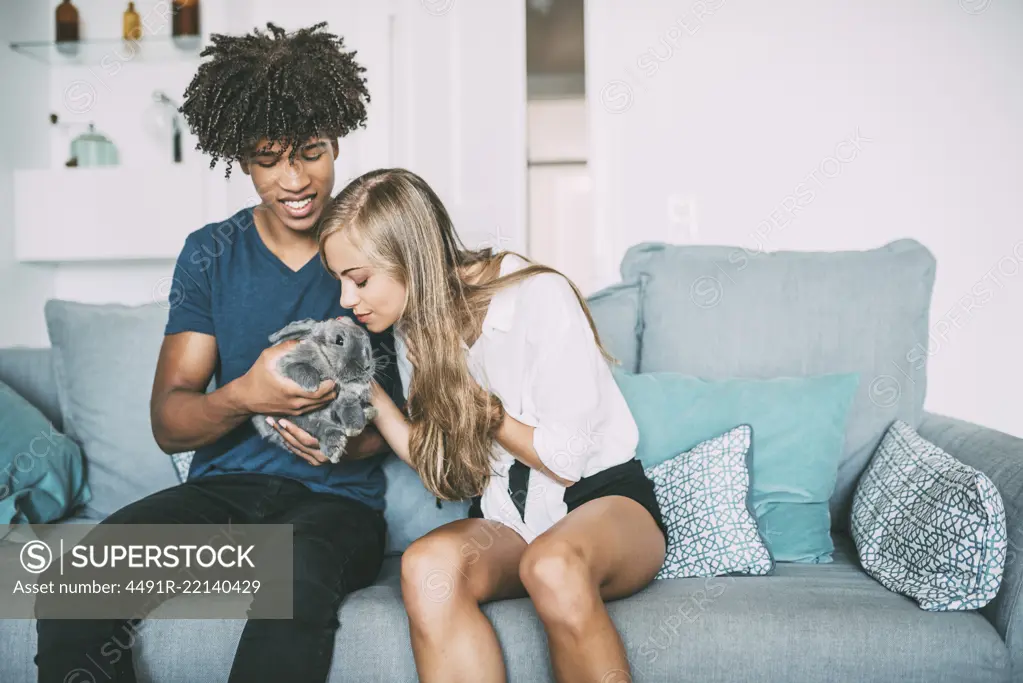 Happy young in love interracial couple relaxed at home caressing a little bunny 