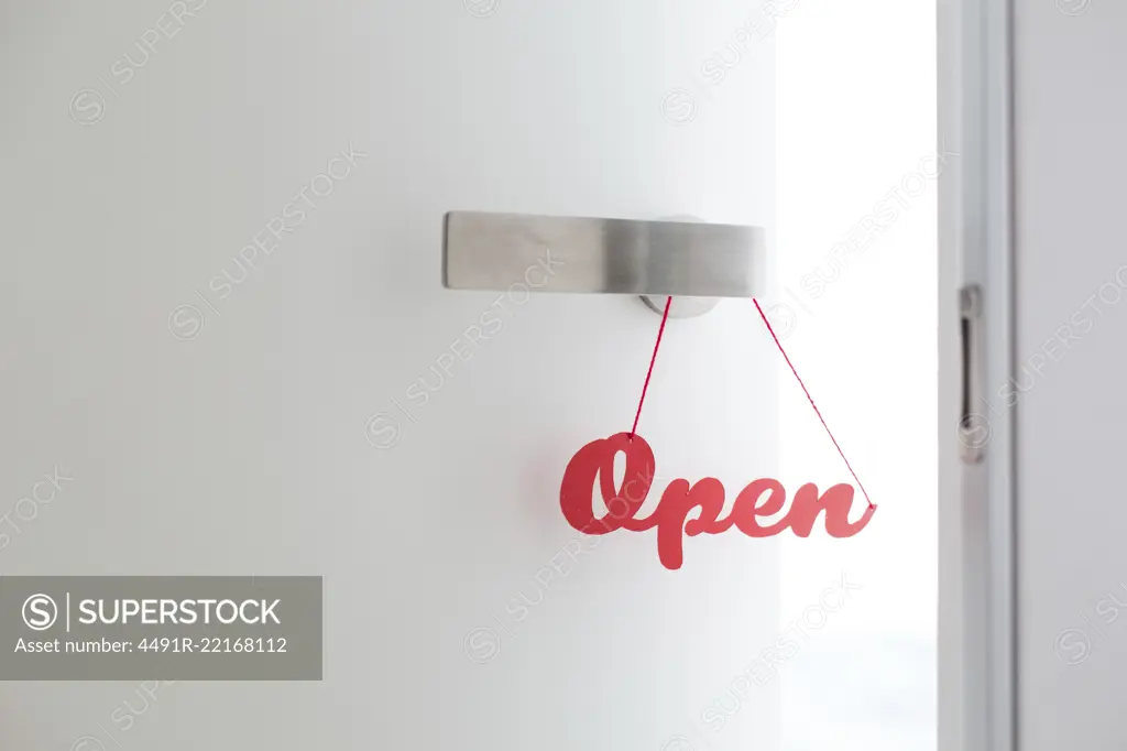 "Open" sign handmade with red letters hanged on a door knob