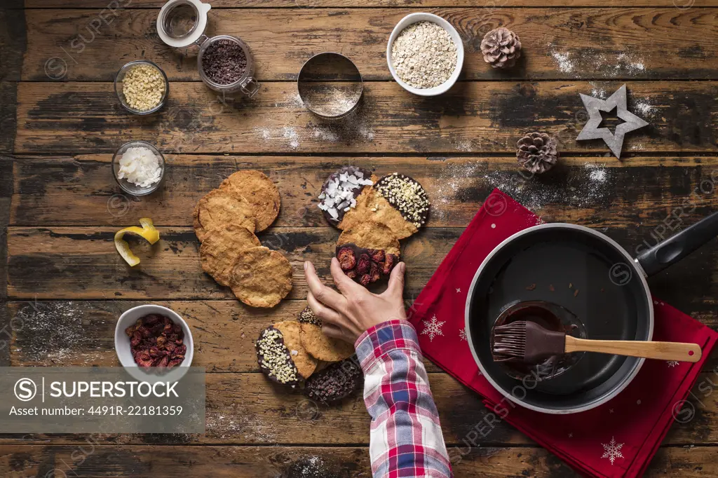 top view of a hand holding christmas cookies on wooden table and ingredients for the recipe