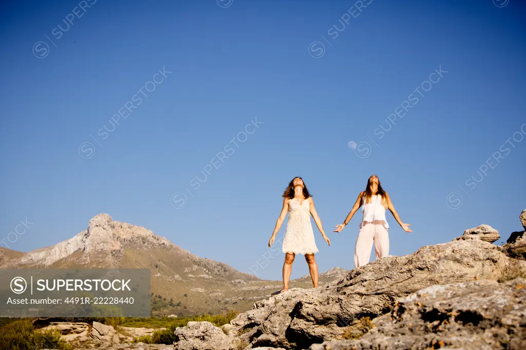 Young mysterious ladies posing on rocks near hill and blue sky with moon