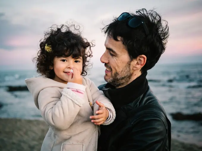 cute scene of dad holding and hugging her little daughter at the beach in winter