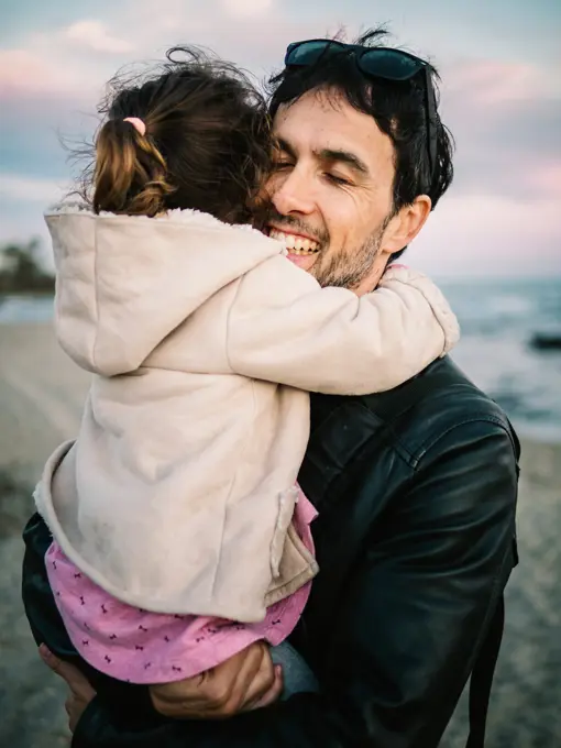 cute scene of dad holding and hugging her little daughter at the beach in winter