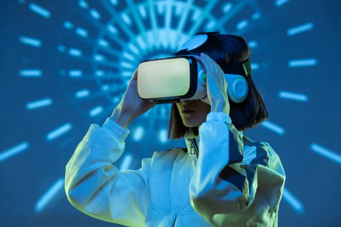Excited young woman having virtual reality experience in neon light
