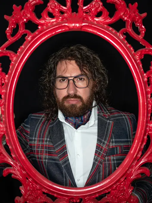Serious impressive well dressed man with curly hair and beard posing in red patterned frame on black background