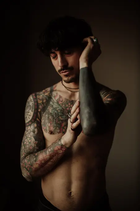 Handsome shirtless tattooed man with mustache and pierced ears and nipples with closed eyes