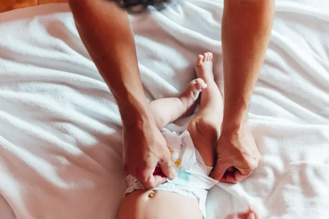 Top view of dad touching legs of newborn infant in diaper lying on bed in house