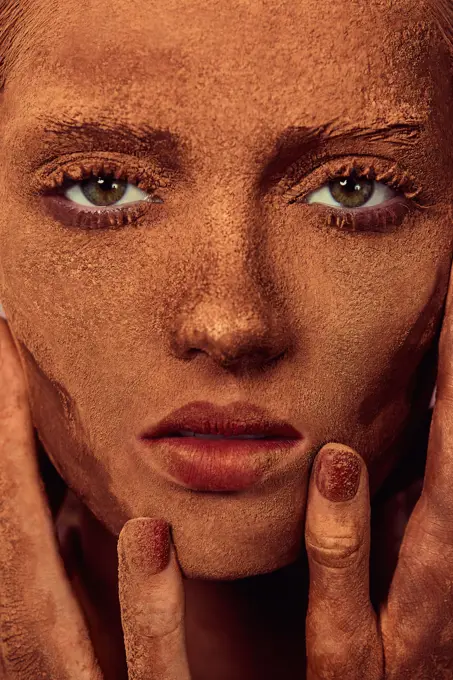 Young beautiful woman with chocolate powder on face touching skin and looking at camera