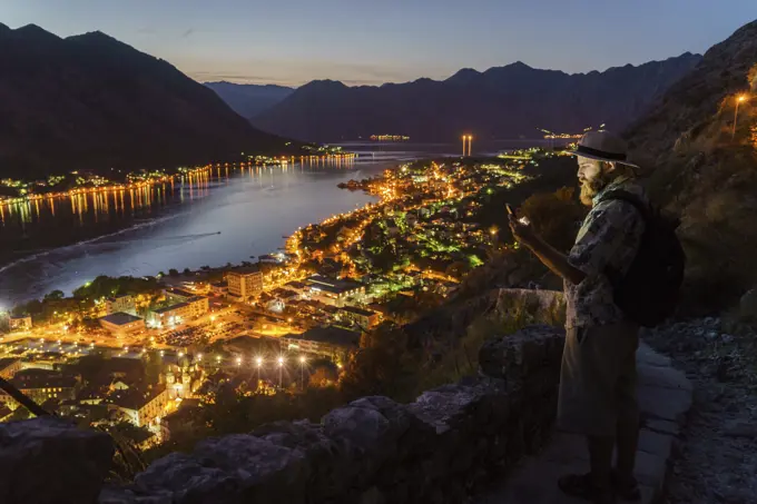 Tourist man using smartphone on mountain at town with illumination at night.
