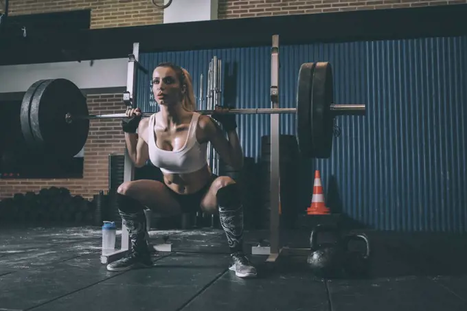 Fit blonde woman training lifting a bar weights in gym 
