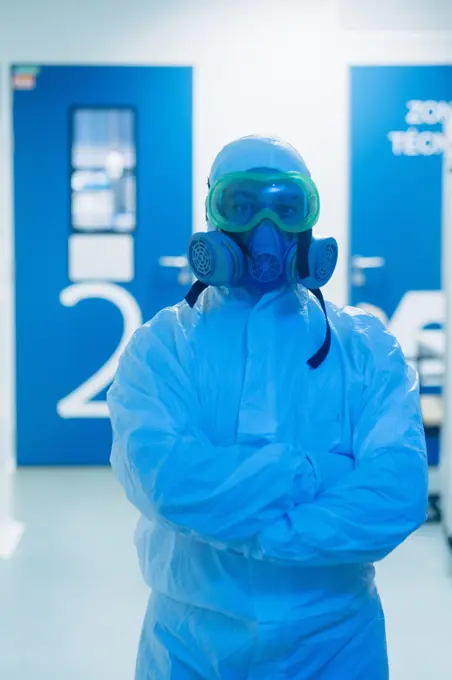 Researcher in white costume looking at camera and standing with arms crossed in laboratory.