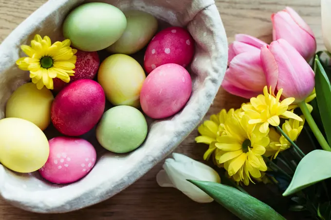Closeup bunch of fresh flowers and basket with colored eggs placed on lumber tabletop