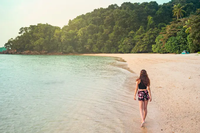 Back view of slim lady walking on sand beach near sea and green tropical forest in Jamaica