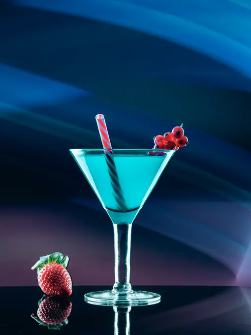 Glass with cocktail and different fresh berries on board on abstract background