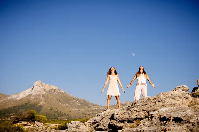 Young mysterious ladies posing on rocks near hill and blue sky with moon