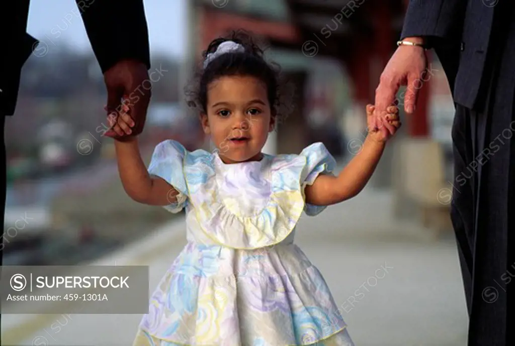 Multiracial girl holding parents' hands