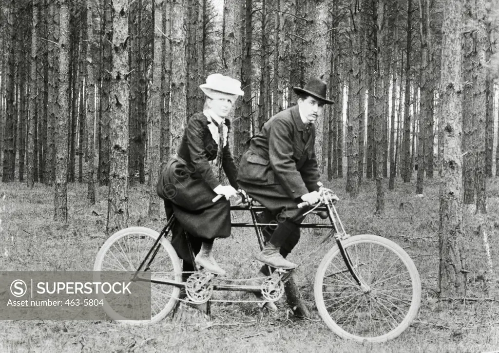 Side profile of a mid adult couple riding a tandem bicycle, 1910