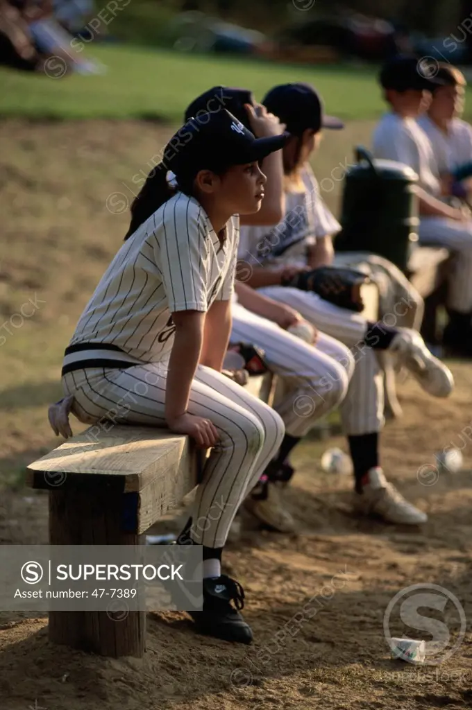 Children sitting on a wooden bench at a baseball game