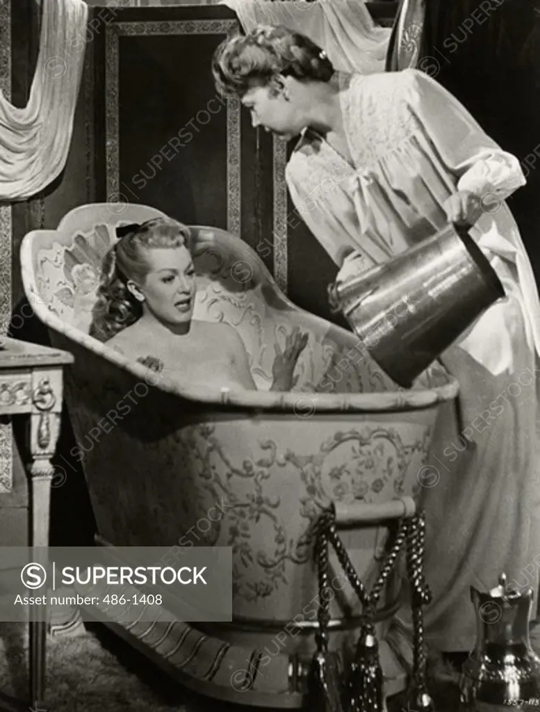 Woman takes bath while servant pours water