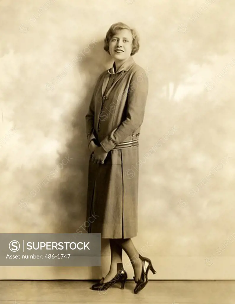 Mid adult woman posing in coat dress by wall, 1931