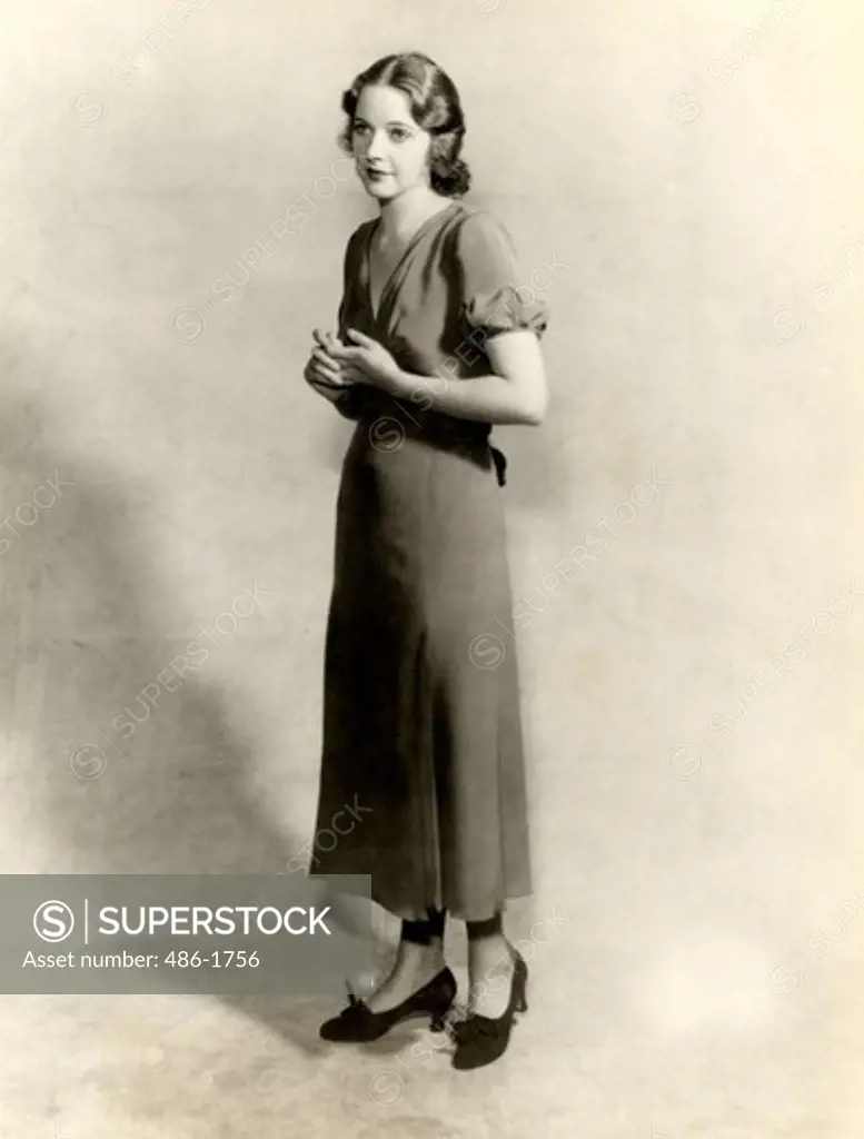 Studio shot of young woman in long dress, hands clasped, 1931