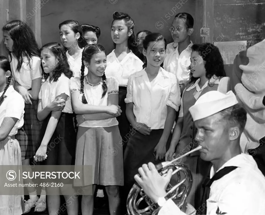 USA, New York City, Chinatown, Crowd Watching Coast Guard Band, Chinatown. Three Girls, Pressed Into Doorway Of The School Building To Make Room For The Coast Guard Band, Watch The Rest Of The Crowd Across The Street.