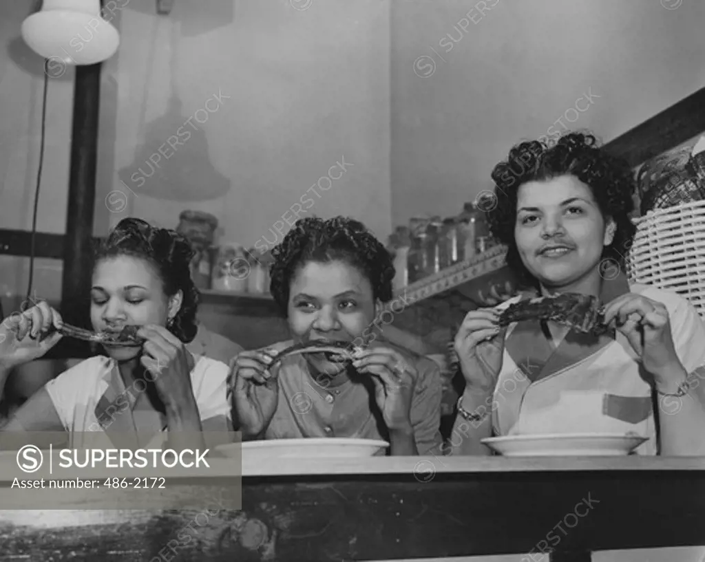 USA, New York City, Harlem, Harlem Speedway, Rib-Eating Competition, Harlem, Harlem Speedway, Approved Technique. Knives And Forks Are Taboo. Fingertips Hold Rib Ends, Daintily. From Left, Jewll Smothers, Pauline Daniels And Laverne Riley. Laverne's Brother Warren Is Owner-Chef Of The Southern Hickory Smoke Bar-B-Q Nook, In Edgecombe Ave.