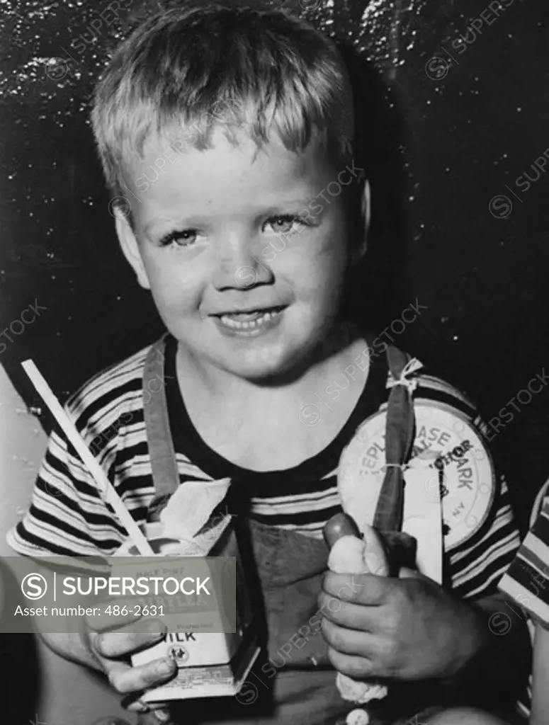 Portrait of smiling boy holding hot dog and milk