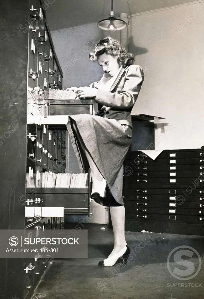 Side profile of a secretary searching files in a filing cabinet