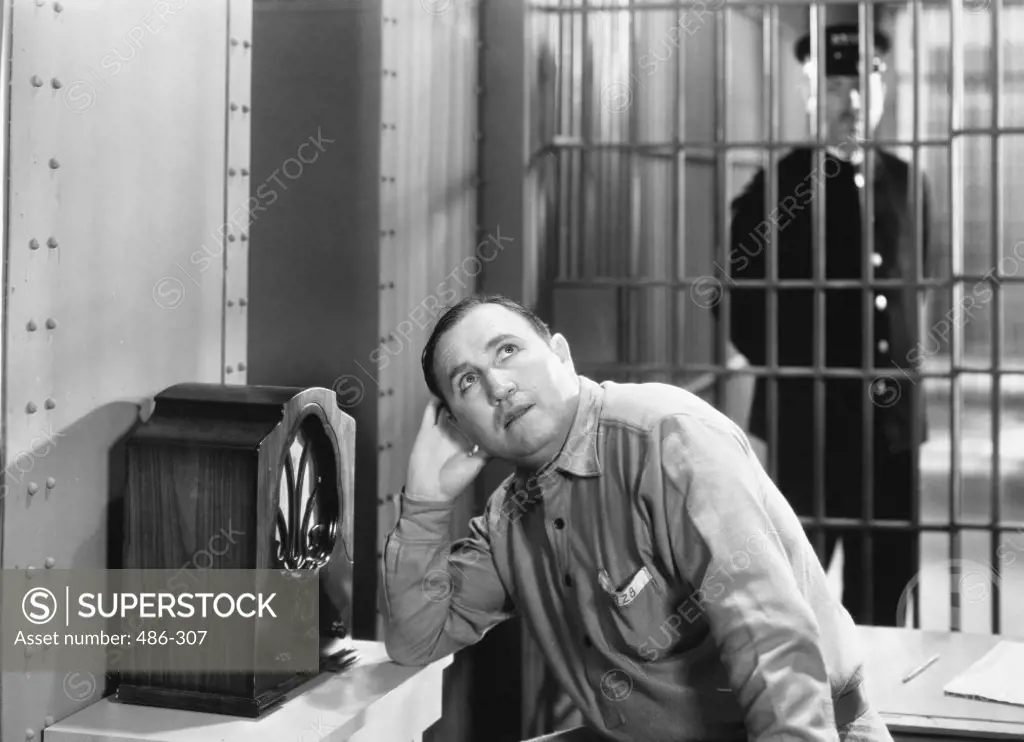 Mid adult man listening a radio in a prison cell