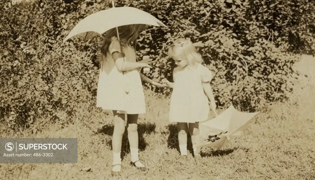 Two girls with umbrellas in garden